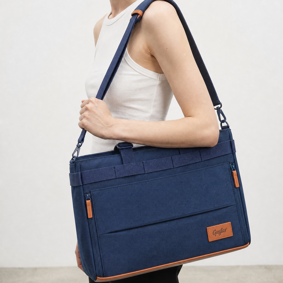 A navy blue canvas shoulder bag with tan leather trim and a matching adjustable strap, carried by a model wearing a white tank top and black pants against a light gray studio background.