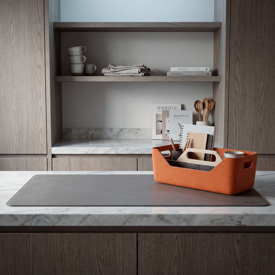 An orange woven office caddy with a handle sits on a gray yoga mat on a white marble countertop in a modern kitchen setting.