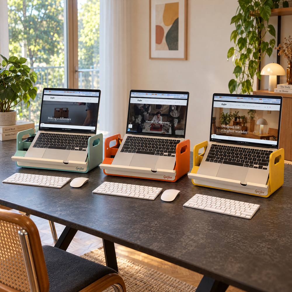 Three laptop desk organizers in light teal, orange, and yellow are shown holding open laptops on a dark wood table in a bright home office setting.