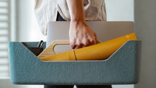 Person holding a yellow FlexMat and laptop in a teal storage bin.